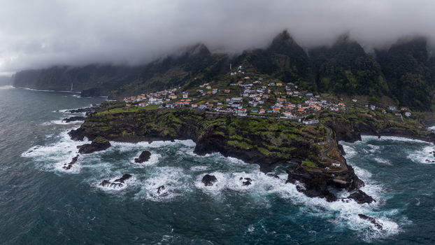 Aerial view of a dramatic coastline where the village nestles against the rugged cliffs under a heavy cloud laden sky Seixal Madeira Portugal.