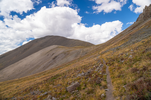 View of the hiking trail leading toward San Luis Peak with rocky slopes and alpine vegetation under a blue sky in Creede Colorado United States. View of the hiking trail leading toward San Luis Peak with rocky slopes and alpine vegetation under a blue sky in Creede Colorado United States.