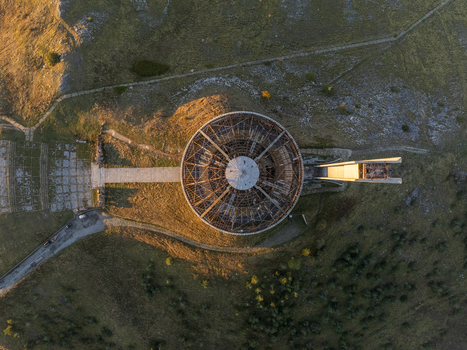 Aerial view of the Buzludzha Monument a circular brutalist structure with exposed framework set against the grassy mountain landscape during golden hour in Stara Zagora Bulgaria. Aerial view of the Buzludzha Monument a circular brutalist structure with exposed framework set against the grassy mountain landscape during golden hour in Stara Zagora Bulgaria.