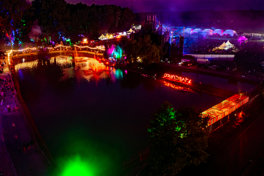 Herzogenaurach Germany 22 July 2022 Aerial view of Open Beatz Festival with colorful stage lights reflecting on the water illuminated tents and crowds of people at night. Herzogenaurach Germany 22 July 2022 Aerial view of Open Beatz Festival with colorful stage lights reflecting on the water illuminated tents and crowds of people at night.