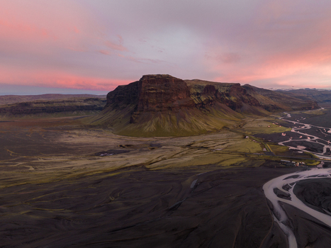 Aerial view of stark black sands contrast with the rugged green mountain under a pastel sky near winding glacial rivers Skaftafell Skaftárhreppur Iceland. Aerial view of stark black sands contrast with the rugged green mountain under a pastel sky near winding glacial rivers Skaftafell Skaftárhreppur Iceland.