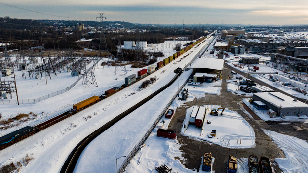 Aerial view of a freight train moving through a snow covered industrial zone with warehouses and power infrastructure Reading Ohio United States. Aerial view of a freight train moving through a snow covered industrial zone with warehouses and power infrastructure Reading Ohio United States.