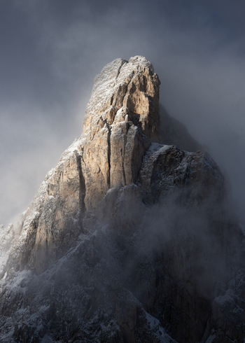 View of a jagged Dolomites mountain peak partially covered in snow and shrouded in dramatic mist and clouds in Trentino Alto Adige Italy. View of a jagged Dolomites mountain peak partially covered in snow and shrouded in dramatic mist and clouds in Trentino Alto Adige Italy.