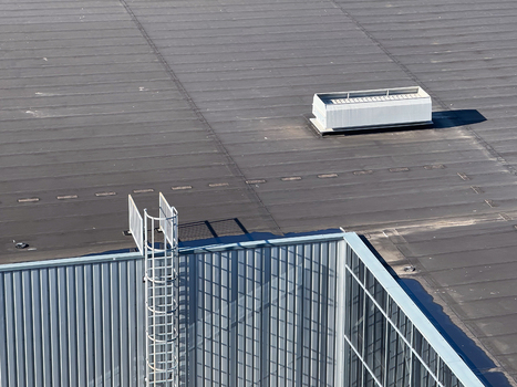 Aerial view of a flat industrial roof featuring a white ventilation unit a metal safety ladder and a glass walled structure in Leeuwarden Friesland Netherlands.