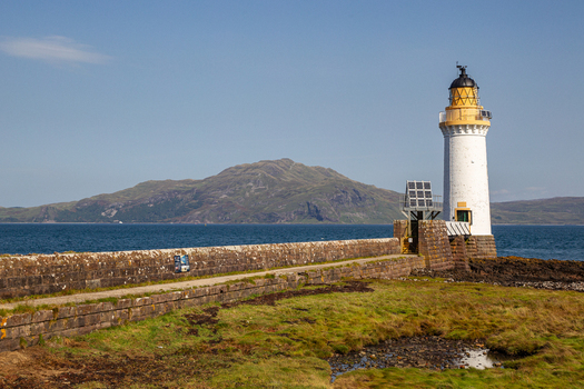 View of Tobermory Lighthouse standing at the end of a stone pier overlooking the sea and distant hills in Isle of Mull Scotland United Kingdom. View of Tobermory Lighthouse standing at the end of a stone pier overlooking the sea and distant hills in Isle of Mull Scotland United Kingdom.