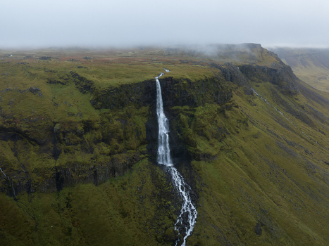 Aerial view of a towering waterfall cascading down a rugged cliff face into a winding stream under a misty sky Snæfellsnes Eyja og Miklaholtshreppur Iceland. Aerial view of a towering waterfall cascading down a rugged cliff face into a winding stream under a misty sky Snæfellsnes Eyja og Miklaholtshreppur Iceland.