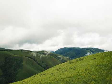 Aerial view of rolling emerald hills disappearing into a soft misty embrace under a vast overcast sky Obudu Cross River Nigeria.
