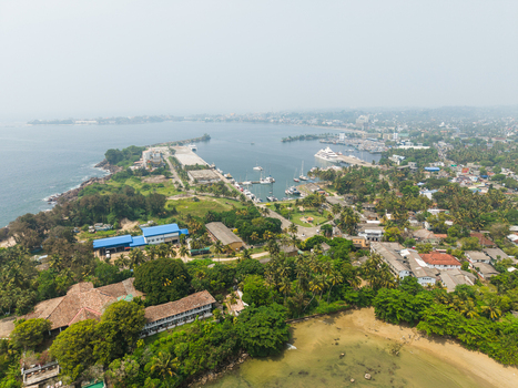 Aerial view of the harbor area near Dewata Beach Road with boats docked at the pier and lush tropical greenery under a hazy sky in Galle Southern Province Sri Lanka.