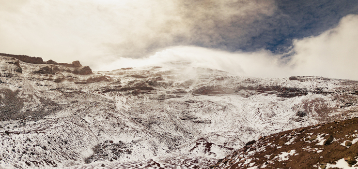 Aerial view of Volcano Chimborazo with its snow covered slopes rocky terrain and swirling clouds at high altitude in Guano Chimborazo Ecuador. Aerial view of Volcano Chimborazo with its snow covered slopes rocky terrain and swirling clouds at high altitude in Guano Chimborazo Ecuador.