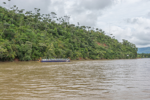 View of a small ferry boat navigating the Sierpe River surrounded by dense tropical rainforest and lush green hills under a cloudy sky in Puntarenas Province Costa Rica. View of a small ferry boat navigating the Sierpe River surrounded by dense tropical rainforest and lush green hills under a cloudy sky in Puntarenas Province Costa Rica.
