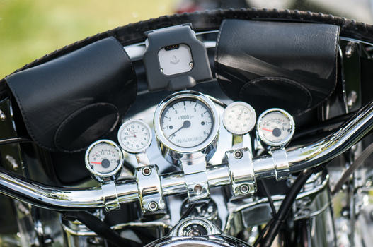 View of a motorcycle dashboard featuring chrome handlebars analog gauges and leather storage pouches in Canada. View of a motorcycle dashboard featuring chrome handlebars analog gauges and leather storage pouches in Canada.