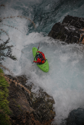 View of a kayaker in a green boat navigating the white water rapids of the Rio Manso surrounded by dark rocks in San Carlos de Bariloche Rio Negro Argentina. View of a kayaker in a green boat navigating the white water rapids of the Rio Manso surrounded by dark rocks in San Carlos de Bariloche Rio Negro Argentina.