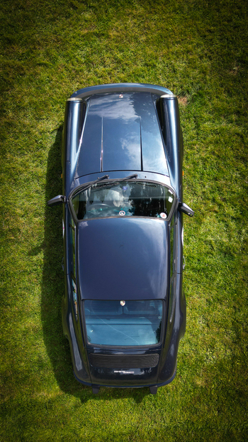 Aerial view of a dark blue classic sports car parked on a lush green lawn with soft sunlight in La Chapelle de Guinchay Bourgogne Franche Comte France.