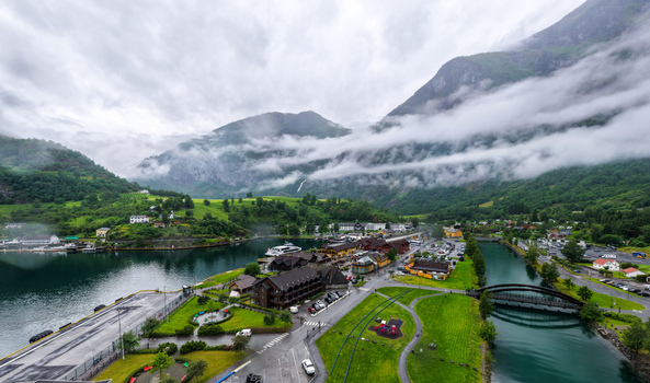 Aerial view of the village of Flam in the Aurlandsfjord featuring wooden buildings a river with a footbridge and green mountains shrouded in low hanging clouds in Flam Vestland Norway. Aerial view of the village of Flam in the Aurlandsfjord featuring wooden buildings a river with a footbridge and green mountains shrouded in low hanging clouds in Flam Vestland Norway.