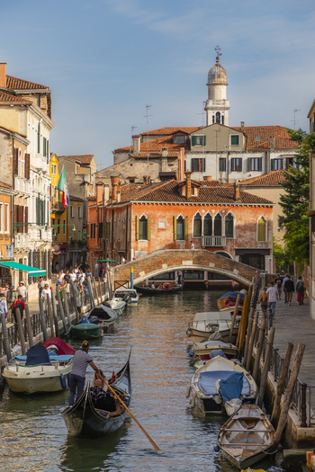 Venice Italy 21 September 2026 View of a canal in Venice with a gondolier rowing a gondola various boats moored along the stone banks and historic buildings under a clear blue sky. Venice Italy 21 September 2026 View of a canal in Venice with a gondolier rowing a gondola various boats moored along the stone banks and historic buildings under a clear blue sky.