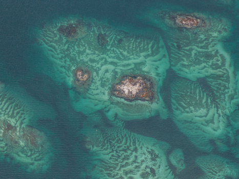 Aerial view of rocky islets surrounded by turquoise shallow waters and intricate sand patterns off the coast of Senja Troms Norway.