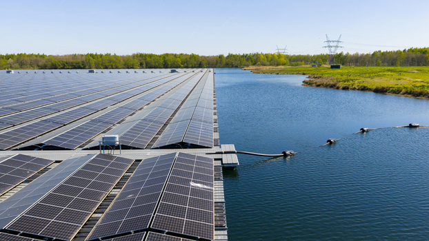 Aerial view of a large floating solar farm on a calm lake surrounded by green fields and lush trees under a clear blue sky Zwolle Overijssel Netherlands. Aerial view of a large floating solar farm on a calm lake surrounded by green fields and lush trees under a clear blue sky Zwolle Overijssel Netherlands.