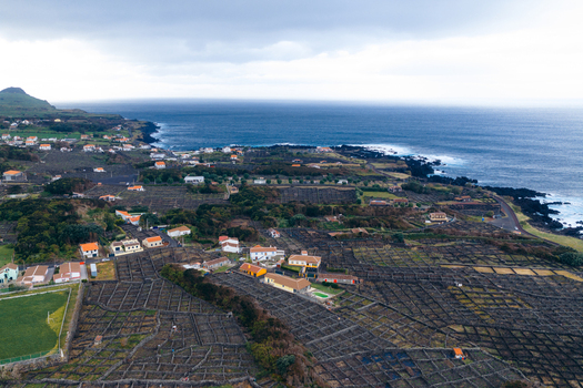 Aerial view of traditional stone walled vineyards and scattered houses along the rugged coastline under a cloudy sky Biscoitos Azores Portugal. Aerial view of traditional stone walled vineyards and scattered houses along the rugged coastline under a cloudy sky Biscoitos Azores Portugal.