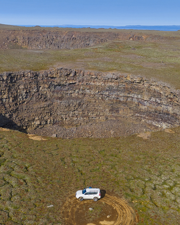 Aerial view of the Litla Viti volcanic crater with its rugged rock walls and a white off road vehicle parked on the mossy terrain in the foreground in Husavik Nordurthing Iceland.