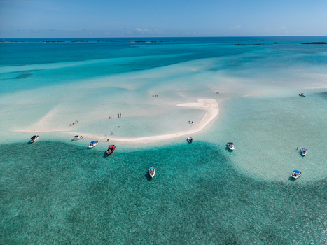 Aerial view of Man O War Cay Sandbar with boats anchored in turquoise waters and people walking on the white sand under a clear sky Rolletown Exuma The Bahamas. Aerial view of Man O War Cay Sandbar with boats anchored in turquoise waters and people walking on the white sand under a clear sky Rolletown Exuma The Bahamas.