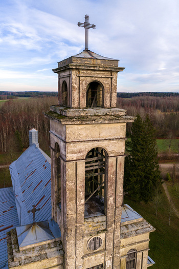 Aerial view of the weathered stone bell tower of Palendriai Monastery with a metal cross on top against a backdrop of autumn forest in Palendriai Siauliu apskritis Lithuania.
