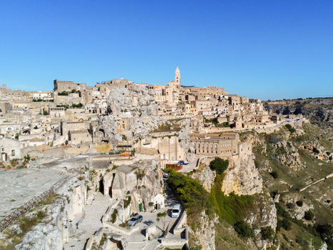 Aerial view of the historic Sassi di Matera with ancient stone cave dwellings narrow streets and a church tower under a clear blue sky in Matera Basilicata Italy.