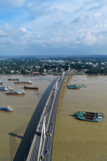 Aerial view of the Shah Amanat Bridge spanning the Karnaphuli River with cargo ships navigating the water and the urban landscape of Chattogram Chittagong Division Bangladesh.