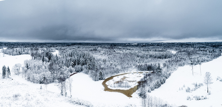 Aerial view of a snow covered forest and a small pond under a cloudy winter sky in Latvia. Aerial view of a snow covered forest and a small pond under a cloudy winter sky in Latvia.