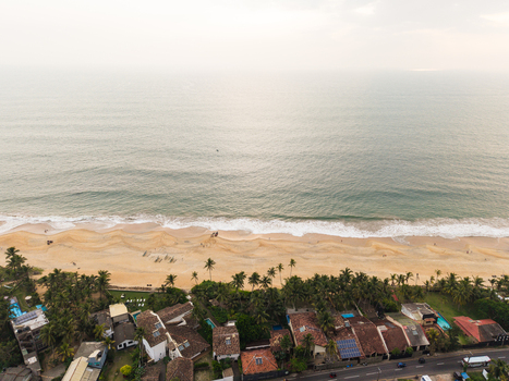 Aerial view of a golden sandy beach lined with palm trees and coastal villas overlooking the Indian Ocean in Galle Southern Province Sri Lanka.