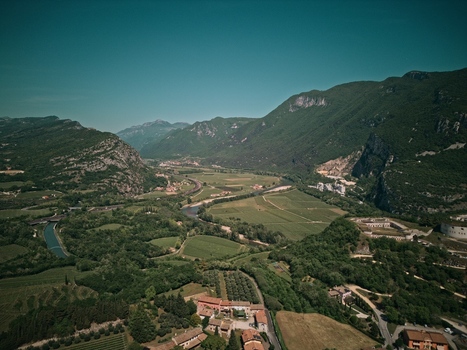Aerial view of the Adige Valley near Lake Garda featuring the winding river lush vineyards and the historic Forte di Rivoli among steep mountains in Italy.