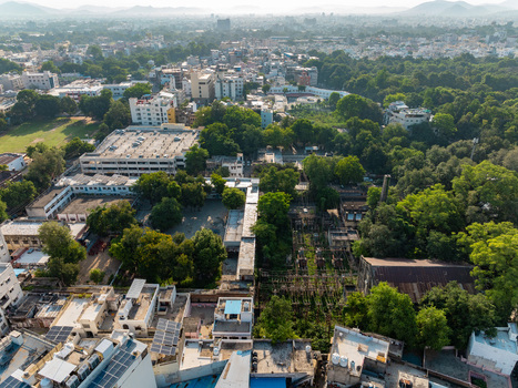 Aerial view of the urban landscape featuring dense residential buildings lush green trees and rooftops under a bright sky in Udaipur Rajasthan India.