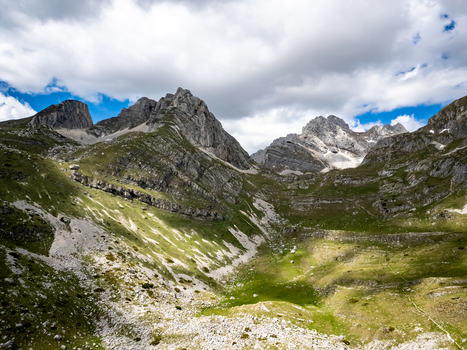 Aerial view of Bobotov Kuk in the rugged Durmitor mountain range featuring dramatic rocky peaks lush green slopes and shifting cloud shadows in Zabljak Municipality Montenegro. Aerial view of Bobotov Kuk in the rugged Durmitor mountain range featuring dramatic rocky peaks lush green slopes and shifting cloud shadows in Zabljak Municipality Montenegro.