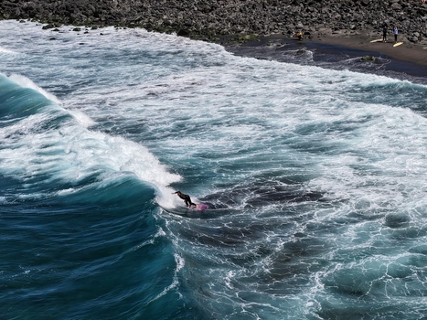 Aerial view of a surfer riding a large turquoise wave near the black sand beach of Praia do Areal de Santa Barbara in Ribeira Grande Acores Portugal. Aerial view of a surfer riding a large turquoise wave near the black sand beach of Praia do Areal de Santa Barbara in Ribeira Grande Acores Portugal.