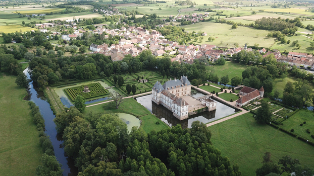 Aerial view of the historic Chateau de Cormatin with its moated castle formal gardens and intricate maze surrounded by lush greenery and the village in Cormatin Bourgogne Franche Comte France. Aerial view of the historic Chateau de Cormatin with its moated castle formal gardens and intricate maze surrounded by lush greenery and the village in Cormatin Bourgogne Franche Comte France.