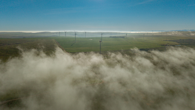 Aerial view of wind turbines standing in a green field partially covered by low hanging morning fog in Vredenburg Western Cape South Africa. Aerial view of wind turbines standing in a green field partially covered by low hanging morning fog in Vredenburg Western Cape South Africa.