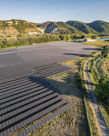 Aerial view of solar photovoltaic panels forming geometric rows at a utility scale solar farm set against rolling hills and a clear sky in Le Pouzin Auvergne Rhone Alpes France. Aerial view of solar photovoltaic panels forming geometric rows at a utility scale solar farm set against rolling hills and a clear sky in Le Pouzin Auvergne Rhone Alpes France.
