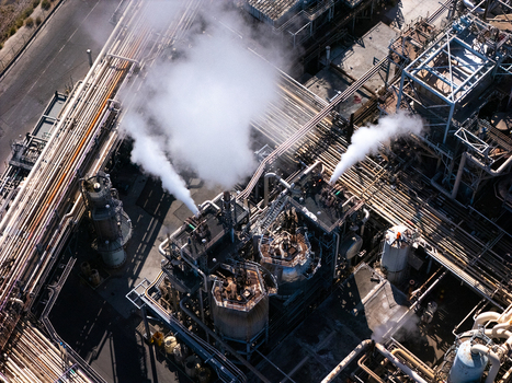 Aerial view of an industrial refinery complex featuring intricate networks of pipes large storage tanks and steam rising from vents in Carson California United States.