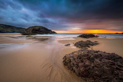 View of Boyeeghter Bay with jagged rocks on the sandy shore under a dramatic sunset sky Ireland.