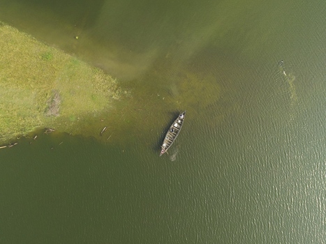 Aerial view of a wooden boat floating on the calm river near a grassy shoreline in Kushtia Khulna Division Bangladesh. Aerial view of a wooden boat floating on the calm river near a grassy shoreline in Kushtia Khulna Division Bangladesh.