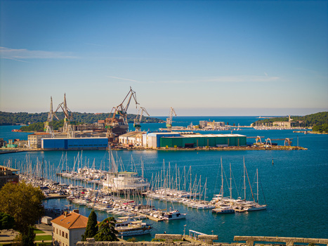 Aerial view of the vibrant harbor dotted with masts of sailboats and the industrial landscape with towering cranes Pula Istria County Croatia.