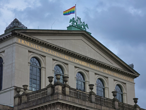 Hanover Germany 29 March 2026 View of the Opernhaus Hannover featuring neoclassical architecture golden inscriptions and a rainbow flag flying under a cloudy sky.