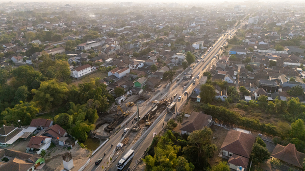 Aerial view of a road construction site with excavators and heavy machinery working on a highway expansion through a dense residential neighborhood in Indonesia. Aerial view of a road construction site with excavators and heavy machinery working on a highway expansion through a dense residential neighborhood in Indonesia.
