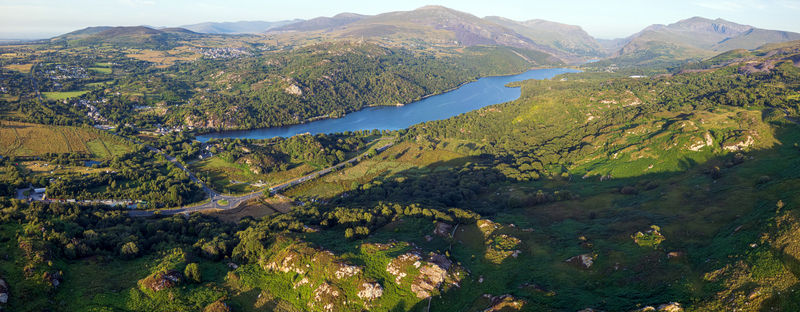 Aerial view of Llyn Padarn and the surrounding mountainous landscape of Snowdonia featuring lush green hills rocky terrain and a winding road near Cwm y glo Wales United Kingdom. Aerial view of Llyn Padarn and the surrounding mountainous landscape of Snowdonia featuring lush green hills rocky terrain and a winding road near Cwm y glo Wales United Kingdom.