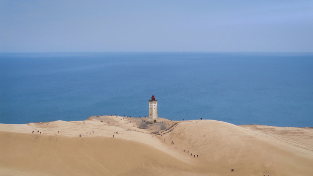 Aerial view of Rubjerg Knude lighthouse surrounded by vast sand dunes and the North Sea with small groups of people walking along the sandy landscape in Hjorring Denmark. Aerial view of Rubjerg Knude lighthouse surrounded by vast sand dunes and the North Sea with small groups of people walking along the sandy landscape in Hjorring Denmark.