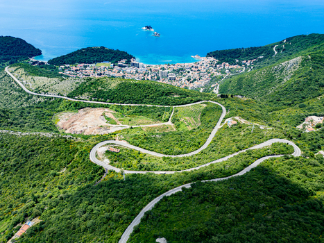 Aerial view of the winding coastal road leading towards the town of Petrovac surrounded by lush green hills and the Adriatic Sea in Petrovac Budva Municipality Montenegro.
