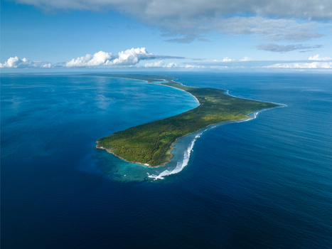 Aerial view of a lush green island fringed by turquoise waters and white crested waves under a serene sky Ouvéa Loyalty Islands Province New Caledonia. Aerial view of a lush green island fringed by turquoise waters and white crested waves under a serene sky Ouvéa Loyalty Islands Province New Caledonia.
