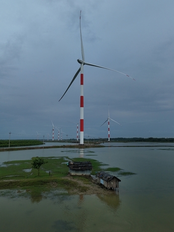 Aerial view of Khurushkul wind farm with red and white turbines standing in flooded fields and small traditional huts in Cox s Bazar Chittagong Division Bangladesh. Aerial view of Khurushkul wind farm with red and white turbines standing in flooded fields and small traditional huts in Cox s Bazar Chittagong Division Bangladesh.
