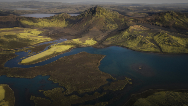 Aerial view of Langisjor lake featuring vibrant green moss covered volcanic hills dark black sand terrain and deep blue water in Vik Myrdalshreppur Iceland. Aerial view of Langisjor lake featuring vibrant green moss covered volcanic hills dark black sand terrain and deep blue water in Vik Myrdalshreppur Iceland.