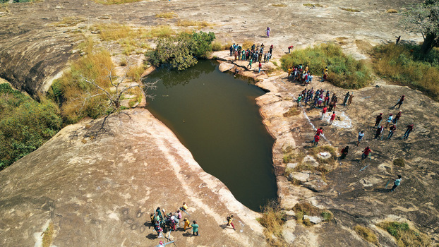 Aerial view of a small lake surrounded by rocky terrain dotted with people and sparse vegetation Jos Nigeria. Aerial view of a small lake surrounded by rocky terrain dotted with people and sparse vegetation Jos Nigeria.
