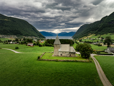 Aerial view of Hove Church surrounded by lush green fields and stone walls with mountains and a fjord in the background in Vik i Sogn Vestland Norway. Aerial view of Hove Church surrounded by lush green fields and stone walls with mountains and a fjord in the background in Vik i Sogn Vestland Norway.